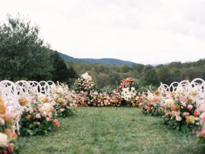 Outdoor ceremony with white chairs and lots of florals on a green lawn with mountain in background