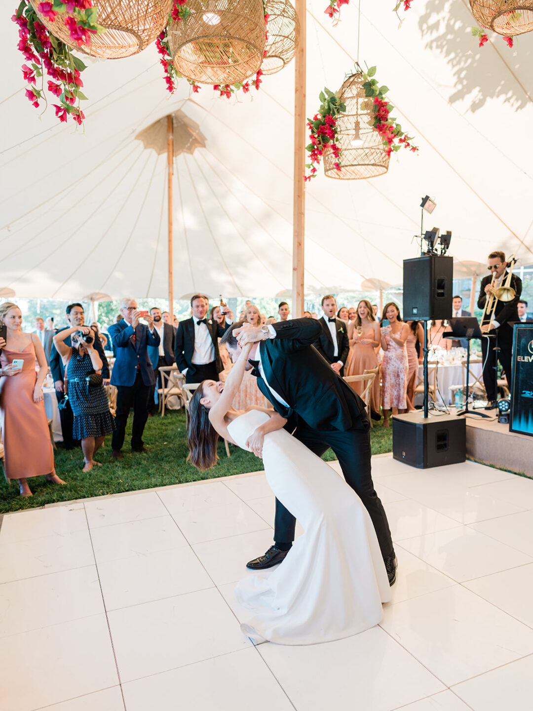 newlyweds dancing under sperry sailcloth tent on white dance floor with rattan chandeliers above 