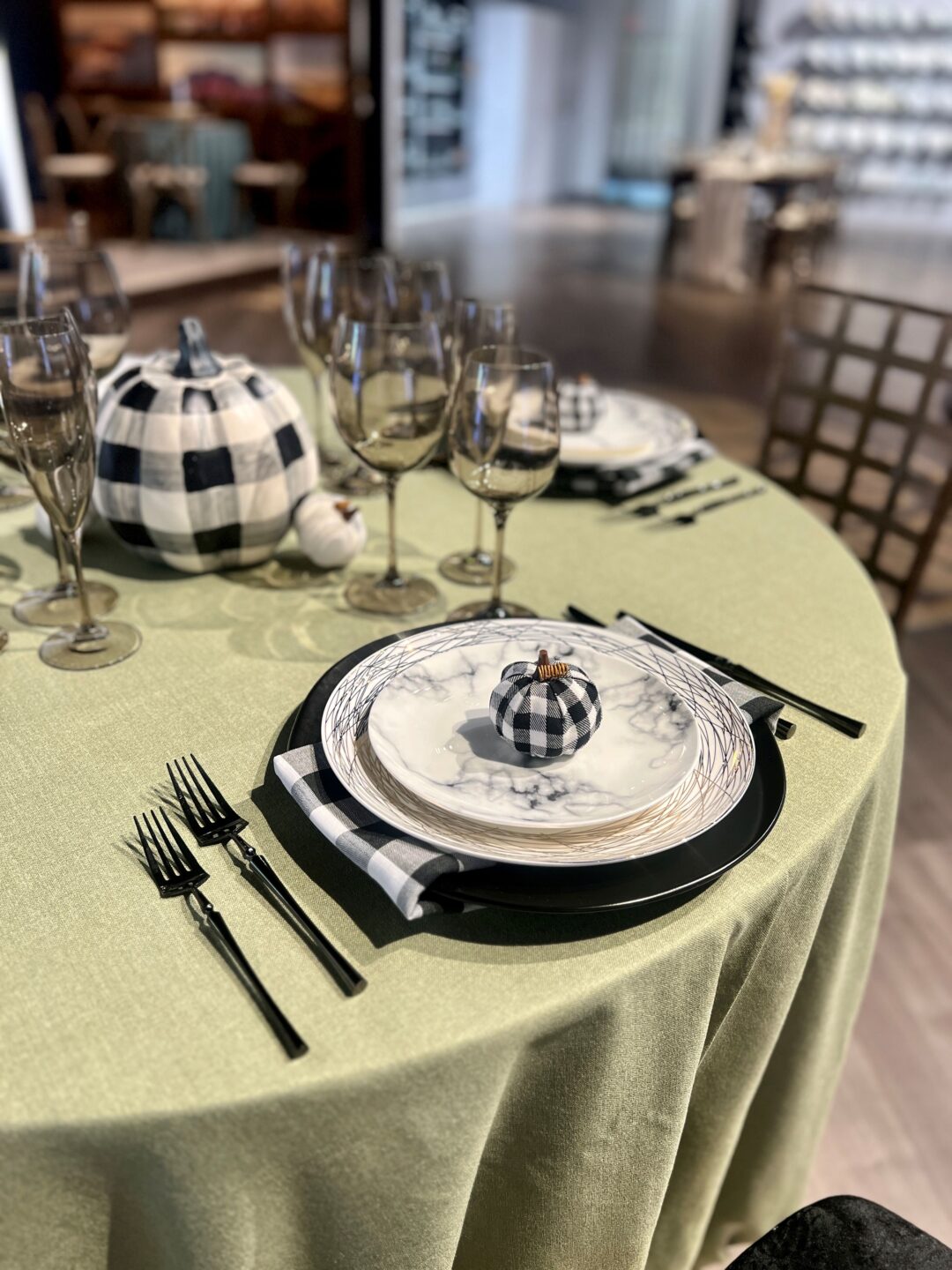 fall tablesetting with greens and black checkered complete with linen, base plates, china,napkins, glassware, flatware and decor of black and white checkered pumpkins